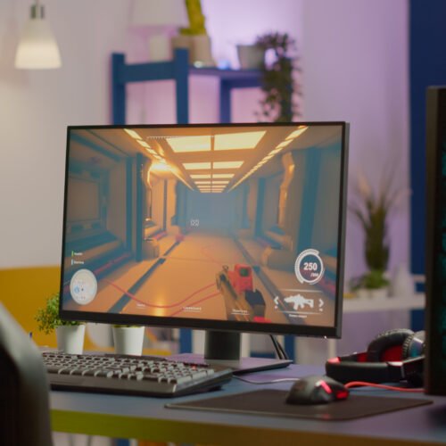Gaming room no people in equiped with RGB powerful personal computer for online videogames tournament and gaming chair, first-person shooter game on screen. Cozy room with neon light.
